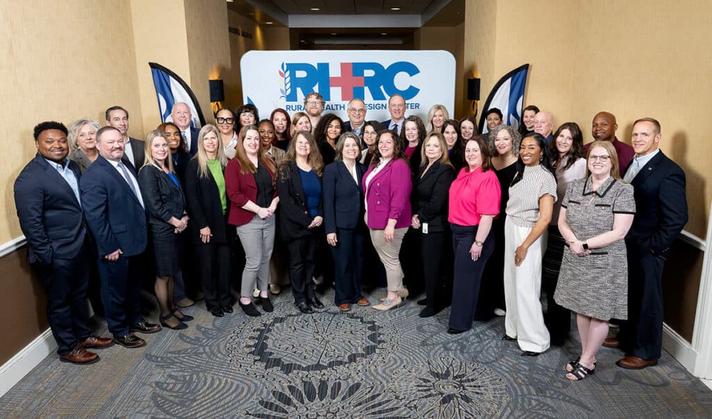A large group of professionals in business attire pose together for a photo in a hotel event hallway.